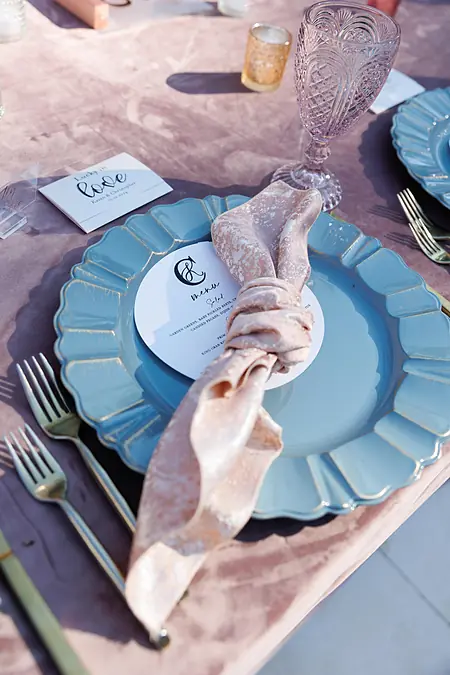 Blue scalloped charger plate with gold rim, blush velvet napkin, and menu card at a Houston wedding