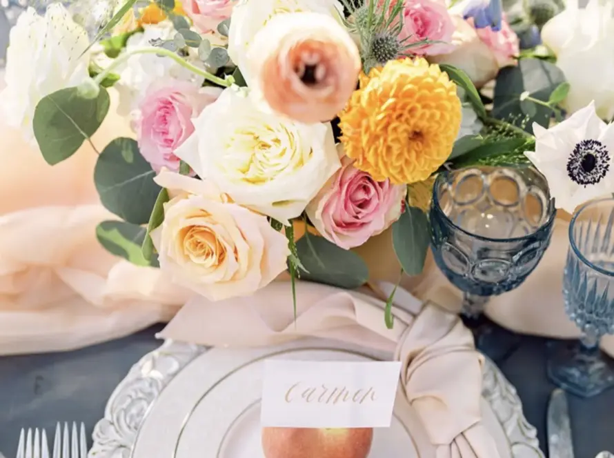 Blush wedding napkin rental with knot fold on a decorative charger, styled with pastel florals and blue goblets