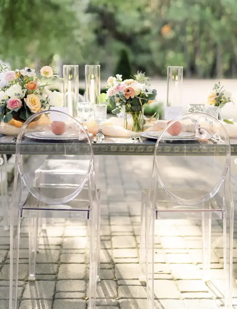Outdoor wedding reception table with blush napkins knotted at each place setting and clear ghost chairs